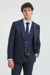 Man wearing a blue checkered suit with a white shirt and blue tie on a light gray background